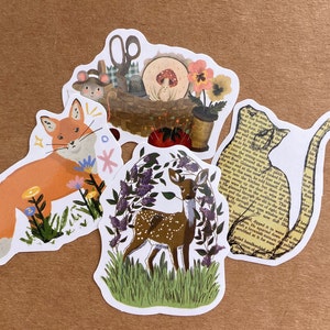 May include: Four illustrated stickers featuring a fox, a deer, a cat, and a sewing kit. The fox is orange and white, the deer is brown with white spots, the cat is yellow with black text, and the sewing kit is brown with red and white accents.