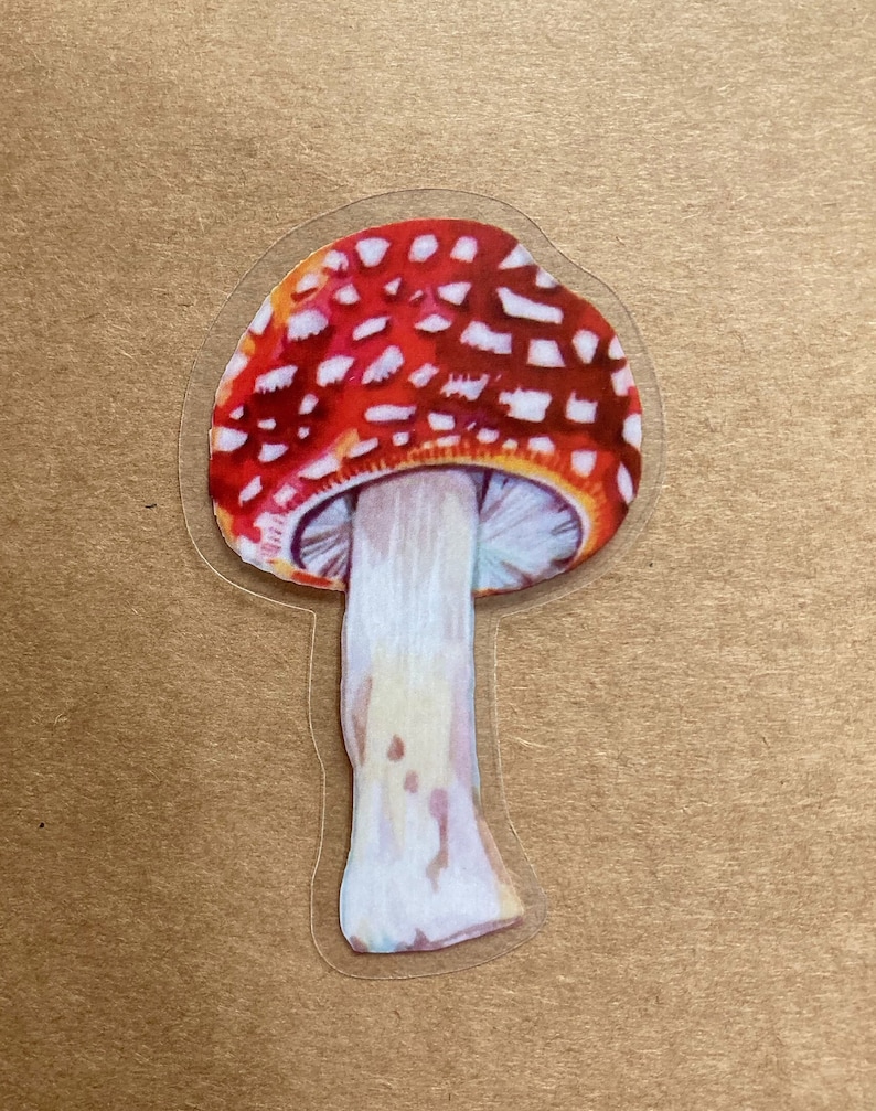 May include: A red and white mushroom sticker with a white stem. The mushroom has a rounded cap with white spots on a red background.