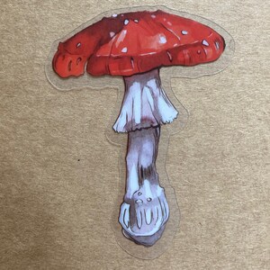 May include: A red and white mushroom sticker with white spots on the cap. The mushroom has a long, slender stem.