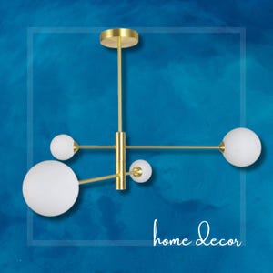 May include: A gold modern chandelier with five white globe-shaped light bulbs. The chandelier has a geometric design with a central rod and three arms extending out.