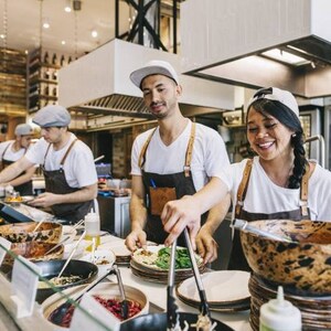 Peut inclure: Trois personnes portant des chemises blanches et des tabliers bruns travaillent dans la cuisine d'un restaurant. Ils préparent des plats et servent les clients. Il y a des bols de nourriture sur le comptoir, ainsi que des assiettes et des ustensiles divers.