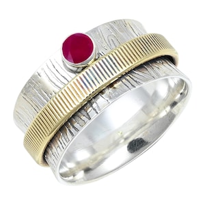May include: A silver spinner ring with a textured surface and a gold-coloured band. A small, round, red gemstone is set on top. The ring has a spinning design, providing a tactile element.