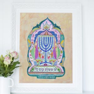 May include: A framed watercolor print featuring a blue menorah with lit candles, surrounded by colorful floral and geometric designs. The artwork is set against a soft, peach-colored background and includes Hebrew text at the bottom.