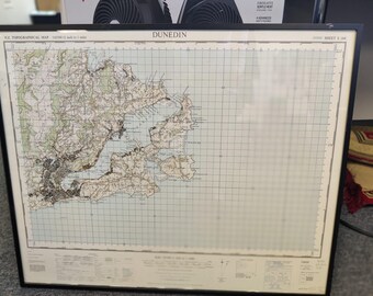 May include: Framed topographical map of Dunedin, New Zealand, with a black frame. The map shows the city's layout, including roads, waterways, and elevation details. The map is labeled "N.Z. Topographical Map" and "Dunedin".