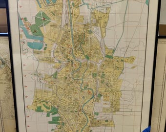 May include: Framed vintage map of Surabaya, Indonesia, with the city name at the top. The map features a detailed layout of the city, including streets, waterways, and green spaces. The map is dated 1963 and is framed in black.