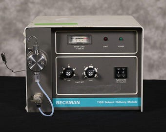 May include: A gray and white Beckman 110B Solvent Delivery Module. It features a pump load gauge, limit and power indicators, and dials for limit set and flow rate. The unit has a stainless steel component on the left side.