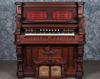May include: A dark wood antique organ with ornate carvings and red fabric accents. The organ features a keyboard, foot pedals, and the text "Lough & Warren Organ Company". The instrument is a vintage piece of musical equipment.