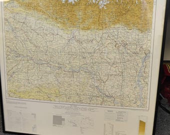 May include: Framed vintage map with a detailed topographical design in shades of tan, beige, and brown. The map is encased in a black frame, offering a classic aesthetic. The map features intricate lines and symbols, suggesting a focus on geographical data.
