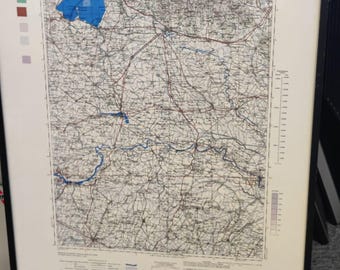 May include: Framed map of Verona, Italy, with detailed road and terrain markings. The map features a blue-colored lake and is labeled "Italy 1:250,000" and "Verona". The map is encased in a black frame.