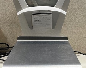 May include: A vintage silver and white mechanical scale with a large dial face. The scale has a rectangular platform and a rounded base. The dial displays weight measurements and a chart. A paper with text is attached to the scale.