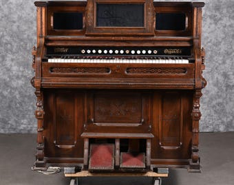May include: Antique wooden pump organ with a dark brown finish. The organ has a keyboard, pedals, and a decorative carved design. The organ is labeled "Miller Organ Co."