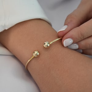 May include: A gold bangle bracelet with two round, textured ends.