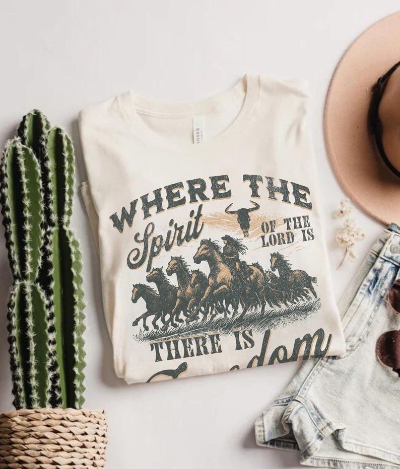 K&ouml;nnte beinhalten: Ein beiges T-Shirt mit einem Vintage-Grafikdruck von rennenden Pferden. Der Text auf dem Shirt lautet "Where the Spirit of the Lord is There is Freedom".