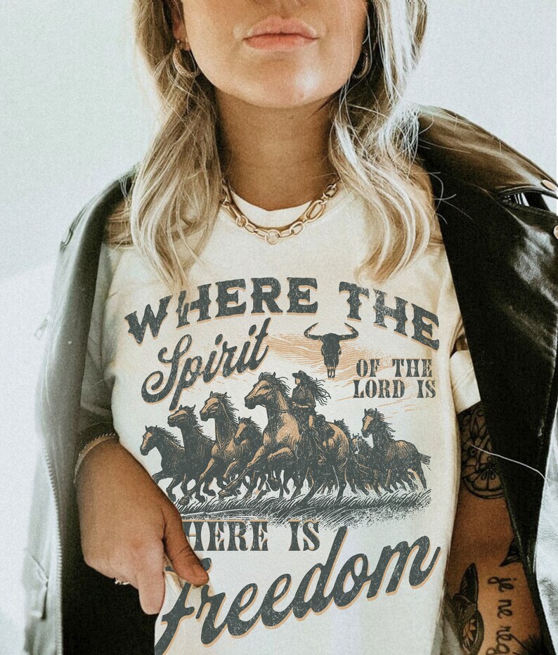 K&ouml;nnte beinhalten: Wei&szlig;es T-Shirt mit einer Grafik einer Gruppe von Pferden, die rennen. Der Text "Where the Spirit of the Lord is there is Freedom" ist auf das T-Shirt gedruckt.