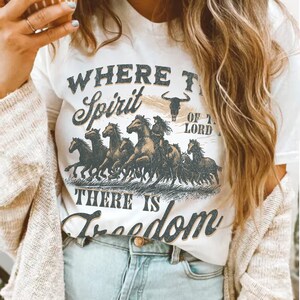 K&ouml;nnte beinhalten: Wei&szlig;es T-Shirt mit einem grafischen Druck einer Herde laufender Pferde mit dem Text "Where the Spirit of the Lord, There is Freedom".