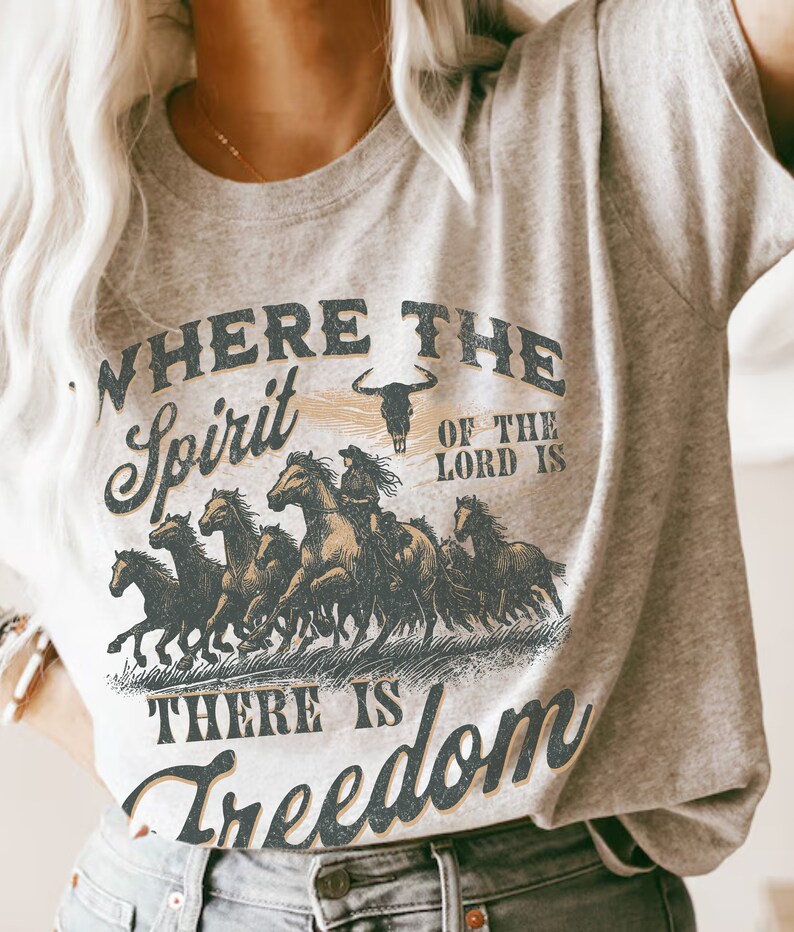 K&ouml;nnte beinhalten: Ein graues T-Shirt mit einem Vintage-Grafikdruck einer galoppierenden Pferdeherde. Der Text auf dem Shirt lautet "Where the Spirit of the Lord is There is Freedom".