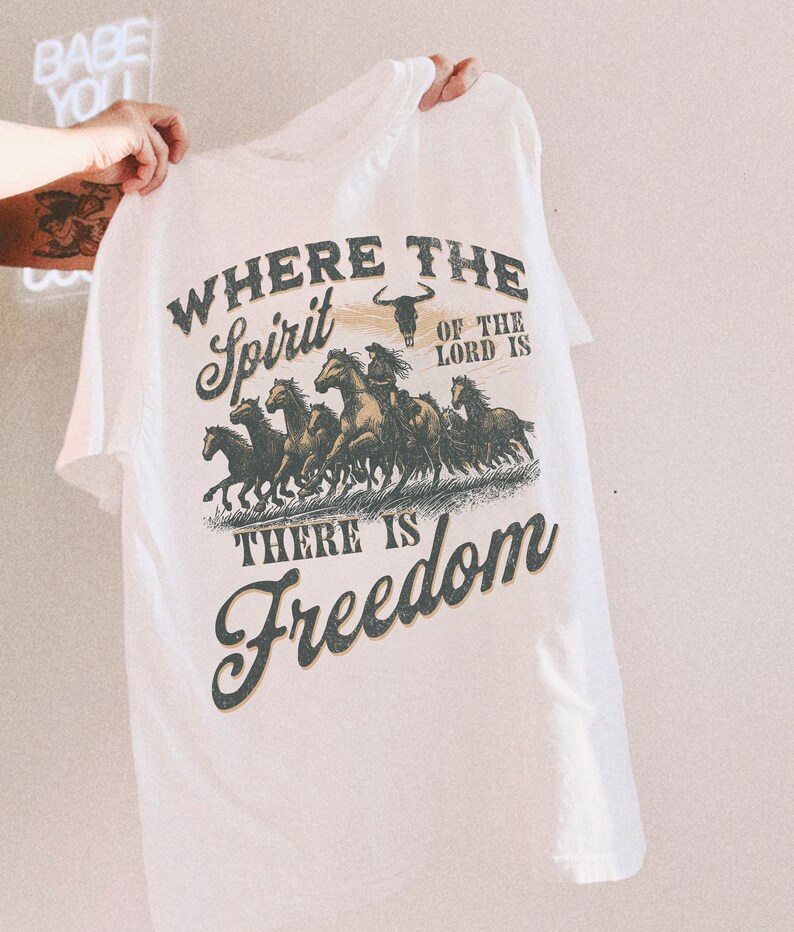 K&ouml;nnte beinhalten: Wei&szlig;es T-Shirt mit einem grafischen Druck einer Herde galoppierender Pferde mit dem Text "Where the Spirit of the Lord is There is Freedom".