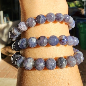 May include: Three stacked bracelets made of dark blue and purple gemstone beads.