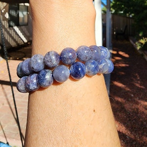 May include: Two blue gemstone bracelets with round beads. The bracelets are stacked on a person's wrist.