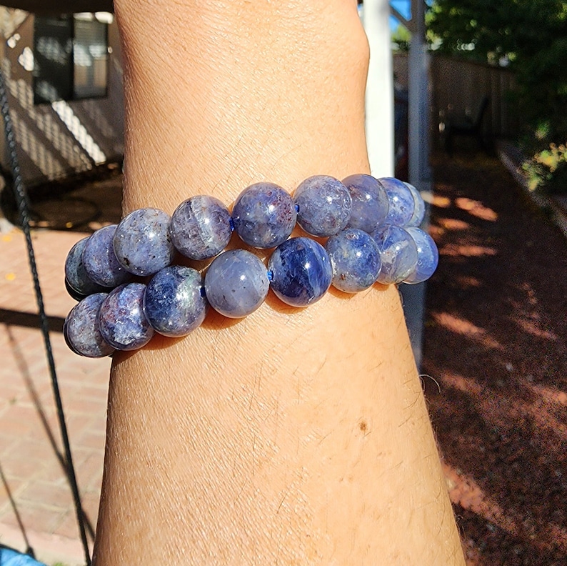 May include: Two blue gemstone bracelets with round beads. The bracelets are stacked on a person's wrist.