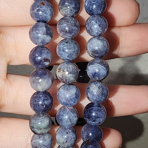May include: Three blue and gray gemstone bracelets with round beads. The bracelets are stacked on top of each other.