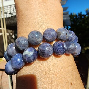 May include: A bracelet made of round, blue-grey gemstone beads. The beads are all approximately the same size and are strung together on a clear elastic cord.