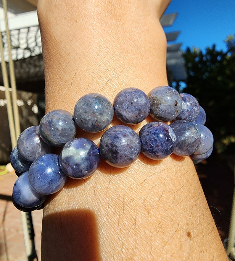 May include: A bracelet made of round, blue-grey gemstone beads. The beads are all approximately the same size and are strung together on a clear elastic cord.