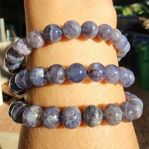 May include: Three stacked bracelets made of blue and gray gemstone beads. The beads are round and have a slightly iridescent finish.