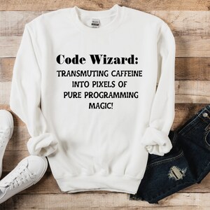 May include: White sweatshirt with the text "Code Wizard: Transmuting caffeine into pixels of pure programming magic!"