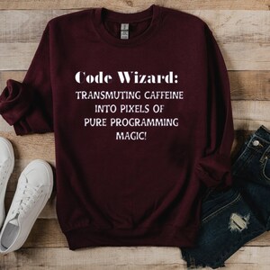 May include: Burgundy sweatshirt with white text that reads "Code Wizard: Transmuting caffeine into pixels of pure programming magic!"