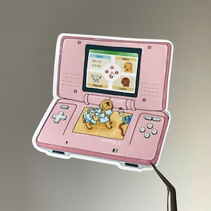 May include: A pink Nintendo DS sticker featuring a cartoon dog taking a bath. The top screen displays a game interface with the date 08/22/2006 and the names Daisy, Manwell, and Lucky. The sticker has a white border.