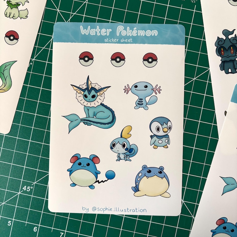 Puede incluir: Una hoja de pegatinas titulada "Water Pok&eacute;mon" con varios personajes de Pok&eacute;mon de tipo agua de dibujos animados en azul, blanco y amarillo. La hoja incluye dise&ntilde;os de Pok&eacute; Ball y la firma del artista.