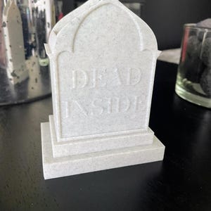 K&ouml;nnte beinhalten: Ein wei&szlig;es, strukturiertes, sargf&ouml;rmiges Objekt mit der Aufschrift "DEAD INSIDE" auf der Vorderseite.
