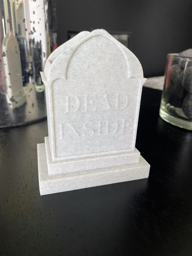 K&ouml;nnte beinhalten: Ein wei&szlig;es, strukturiertes, sargf&ouml;rmiges Objekt mit der Aufschrift "DEAD INSIDE" auf der Vorderseite.