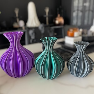 May include: Three decorative vases with a pleated design. The vases are purple, teal, and grey.