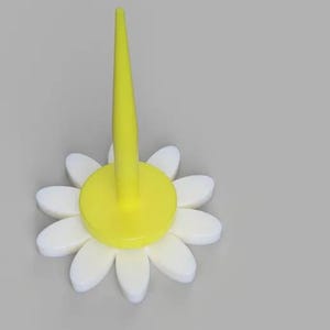 May include: A yellow plastic flower with white petals and a yellow center. The flower has a tall, pointed yellow stem.