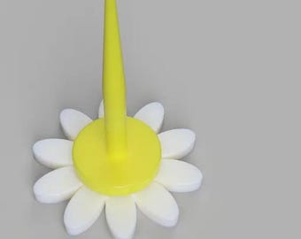 Könnte beinhalten: Eine gelbe Plastikblume mit weißen Blütenblättern und einer gelben Mitte. Die Blume hat einen hohen, spitzen gelben Stiel.
