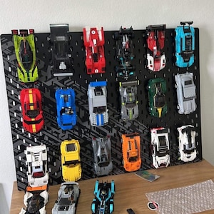 May include: A collection of 19 miniature toy cars displayed on a black pegboard. The cars are in various colors, including red, blue, green, yellow, white, and black. Some of the cars have racing stripes or other details. The cars are arranged in rows on the pegboard, with some cars on the bottom shelf.