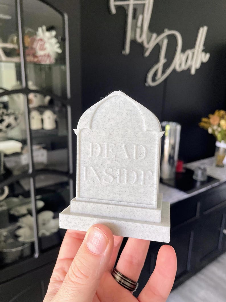 K&ouml;nnte beinhalten: Eine kleine, wei&szlig;e, sargf&ouml;rmige Dekoration mit der Aufschrift "DEAD INSIDE" auf der Vorderseite. Die Dekoration wird in der Hand einer Person gehalten.