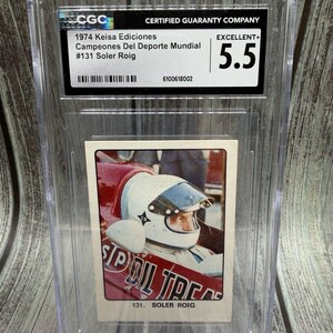May include: A 1974 Keisa Ediciones Campeones Del Deporte Mundial trading card, featuring Soler Roig. The card is graded Excellent+ 5.5 by Certified Guaranty Company and encased in a protective holder. The card shows a race car driver in a helmet.