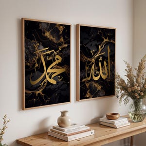 May include: Two framed art prints featuring gold Arabic calligraphy on a black and gold marble background. The frames are a light brown color. The print on the left says "Muhammad" and the print on the right says "Allah".