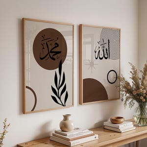 Puede incluir: Dos impresiones artísticas enmarcadas con fondos beige y marcos de madera. Una presenta un círculo marrón con caligrafía árabe negra y un diseño de hojas negras. La otra tiene caligrafía árabe negra, una estrella y círculos concéntricos.