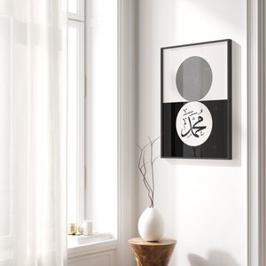 Peut inclure: Impression d'art minimaliste noir et blanc avec un cercle aux anneaux concentriques et une calligraphie arabe dans un cercle sur fond noir. L'impression est encadr&eacute;e dans un cadre noir et accroch&eacute;e &agrave; un mur blanc.