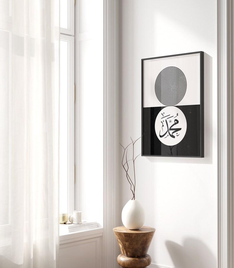Peut inclure: Impression d'art minimaliste noir et blanc avec un cercle aux anneaux concentriques et une calligraphie arabe dans un cercle sur fond noir. L'impression est encadr&eacute;e dans un cadre noir et accroch&eacute;e &agrave; un mur blanc.