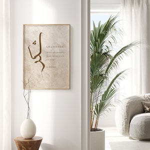 May include: A beige framed print with a brown calligraphy design and the text "Gratitude" and a quote from the Quran. The print is hanging on a white wall in a modern interior.