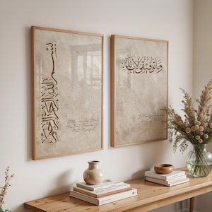 Puede incluir: Dos impresiones artísticas enmarcadas con caligrafía árabe en tinta marrón sobre un fondo beige texturizado. Las impresiones están en marcos de madera marrón claro. El texto incluye frases en árabe e inglés. Las impresiones se exhiben sobre una mesa de madera marrón claro.