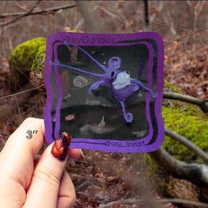 May include: A purple square art print featuring an octopus with the text "Stay Curious" and "@sea_fineart". The print is 3 inches in size. The octopus is depicted in a whimsical style with a light blue object on its head.