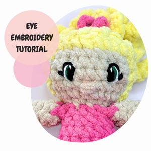 Peut inclure: Gros plan sur une poupée en crochet avec des cheveux en laine blonde, une robe rose et des yeux brodés verts. Le texte "EYE EMBROIDERY TUTORIAL" est dans un cercle rose.