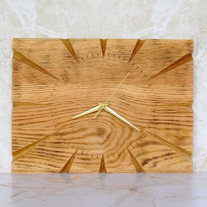Peut inclure: Une horloge murale en bois avec des aiguilles dorées et un design unique. Le cadran de l'horloge est en bois avec un motif de grain et a un design en forme de soleil.