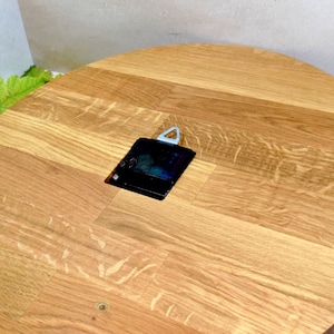May include: A round wooden clock face with a black clock mechanism. The clock face is made of light brown wood with a grain pattern.